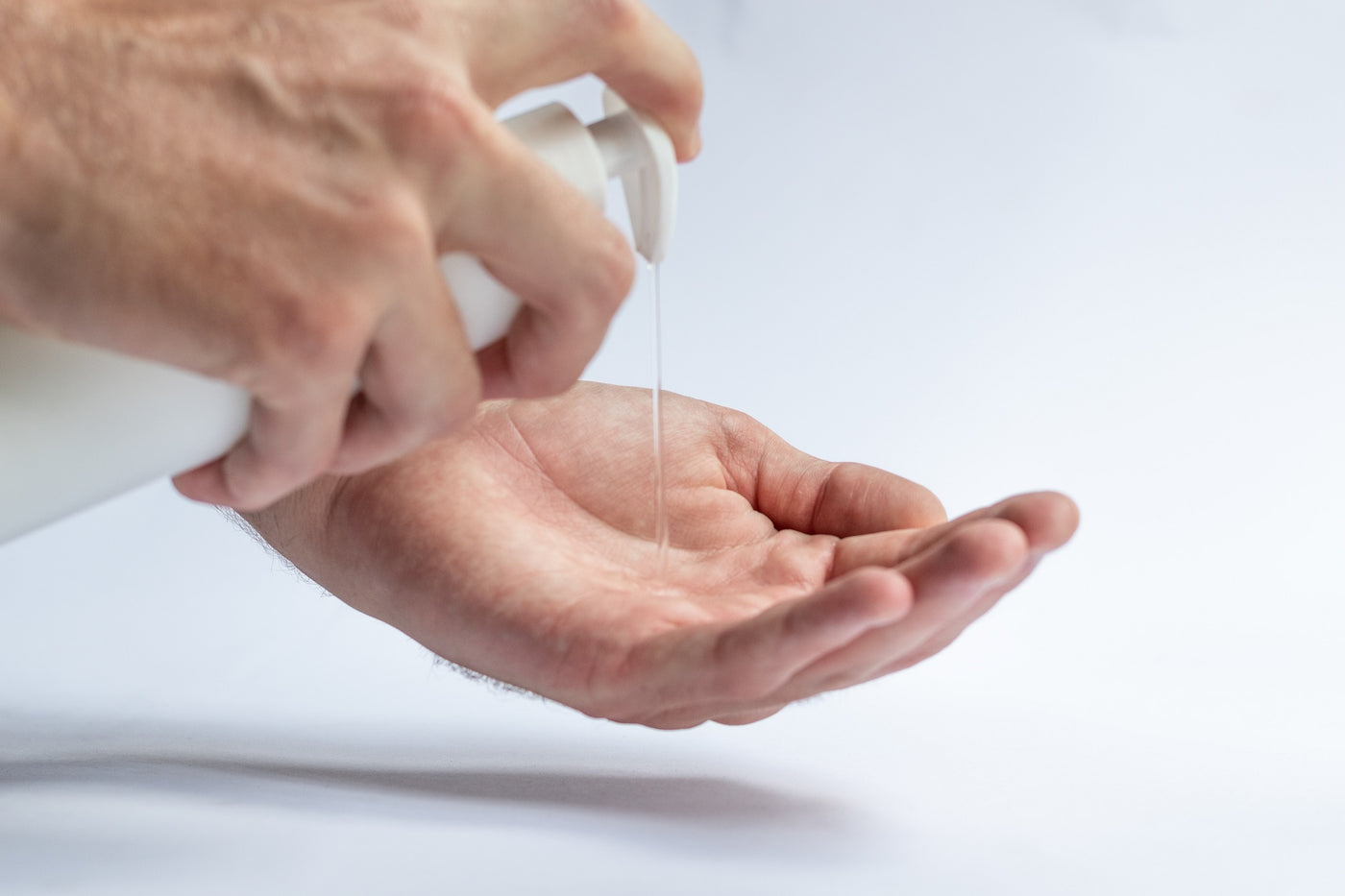Männerhand, die transparente Flüssigseife aus einem Dosierspender in die Handflächen giesst.